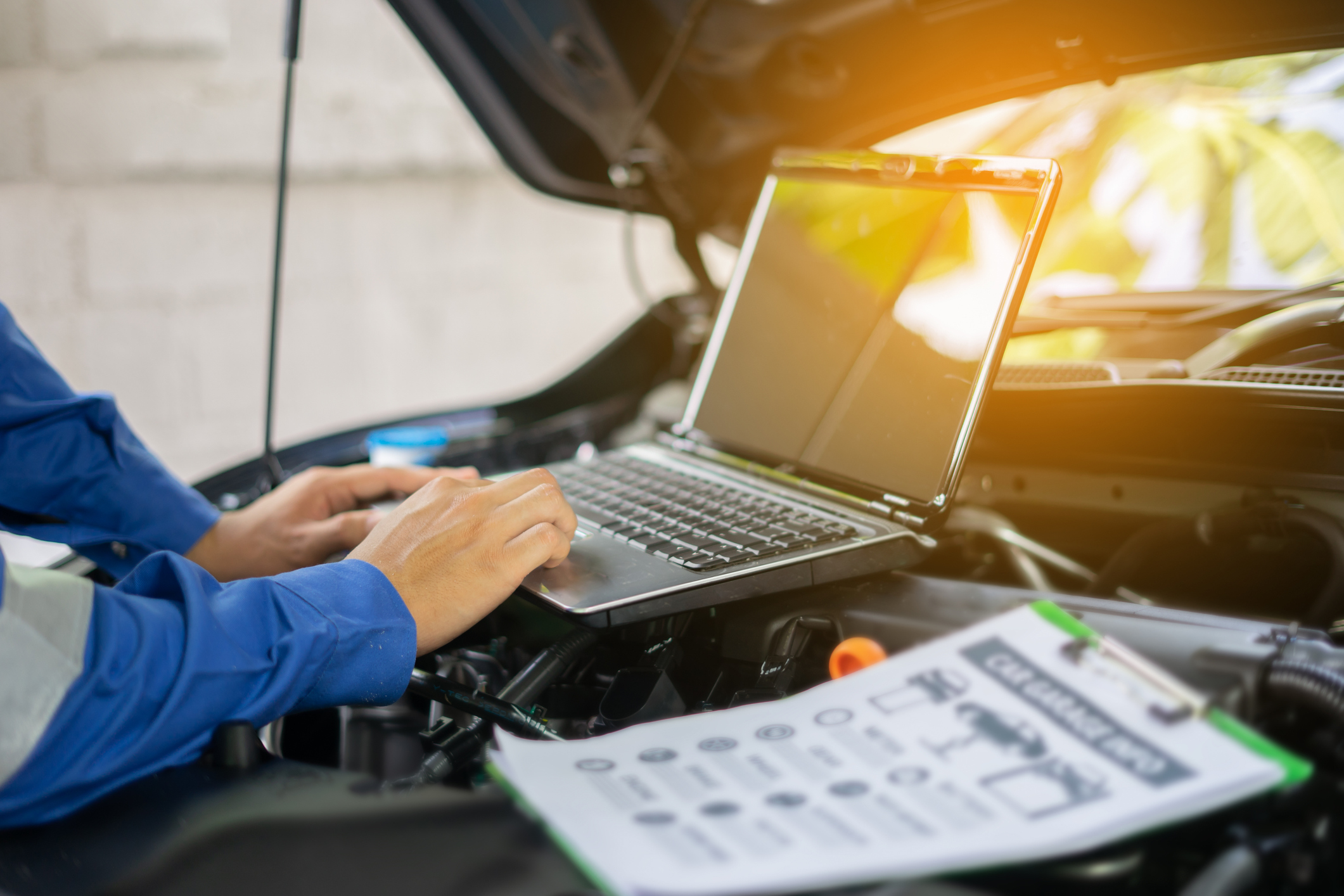 car service, repair, maintenance concept – auto mechanic man or Smith writing to the clipboard at warehouse workshop, technician doing the checklist for repairs engine a car in the garage with laptop